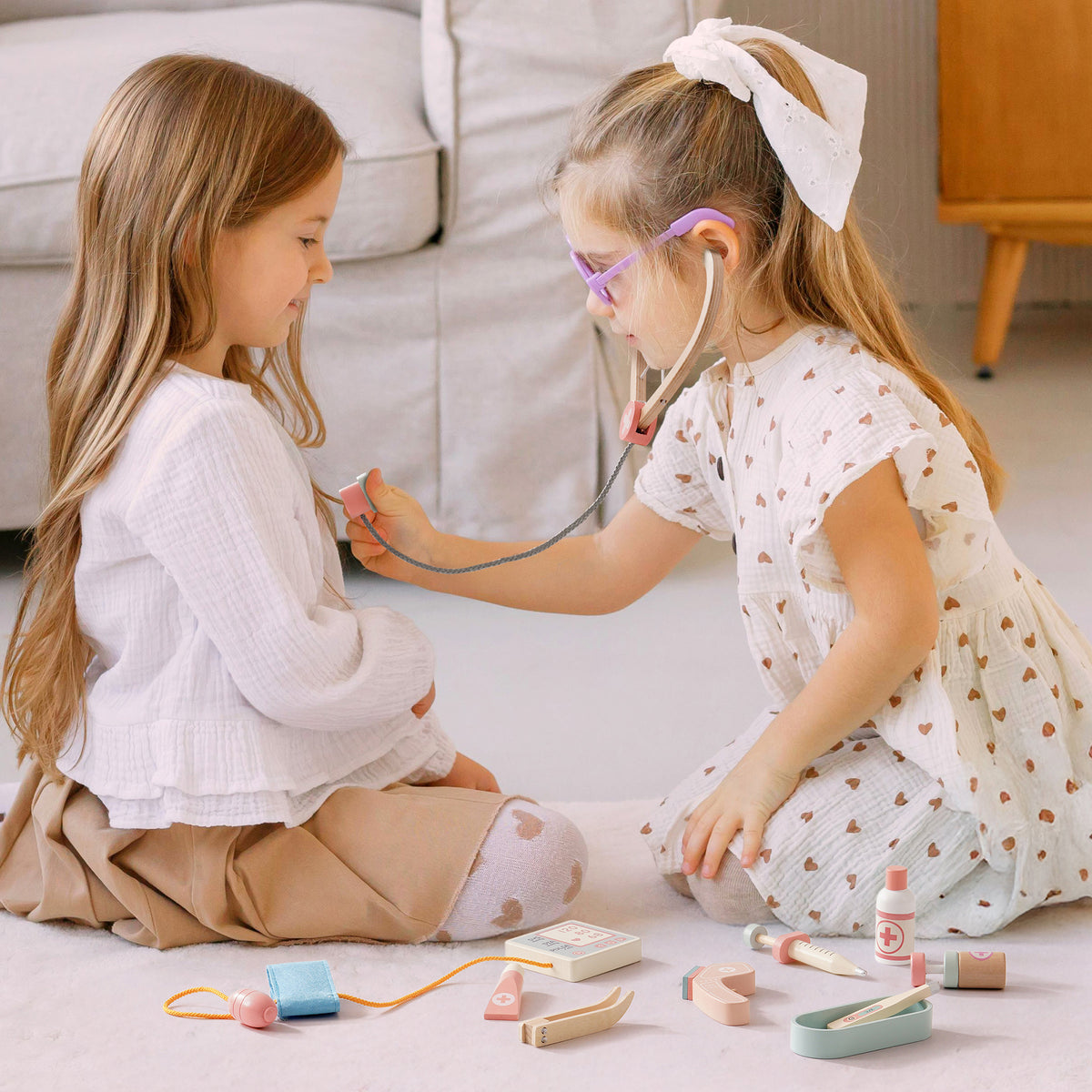 Two girls taking turns using a stethoscope in imaginative doctor play with the ROBUD wooden medical activity set