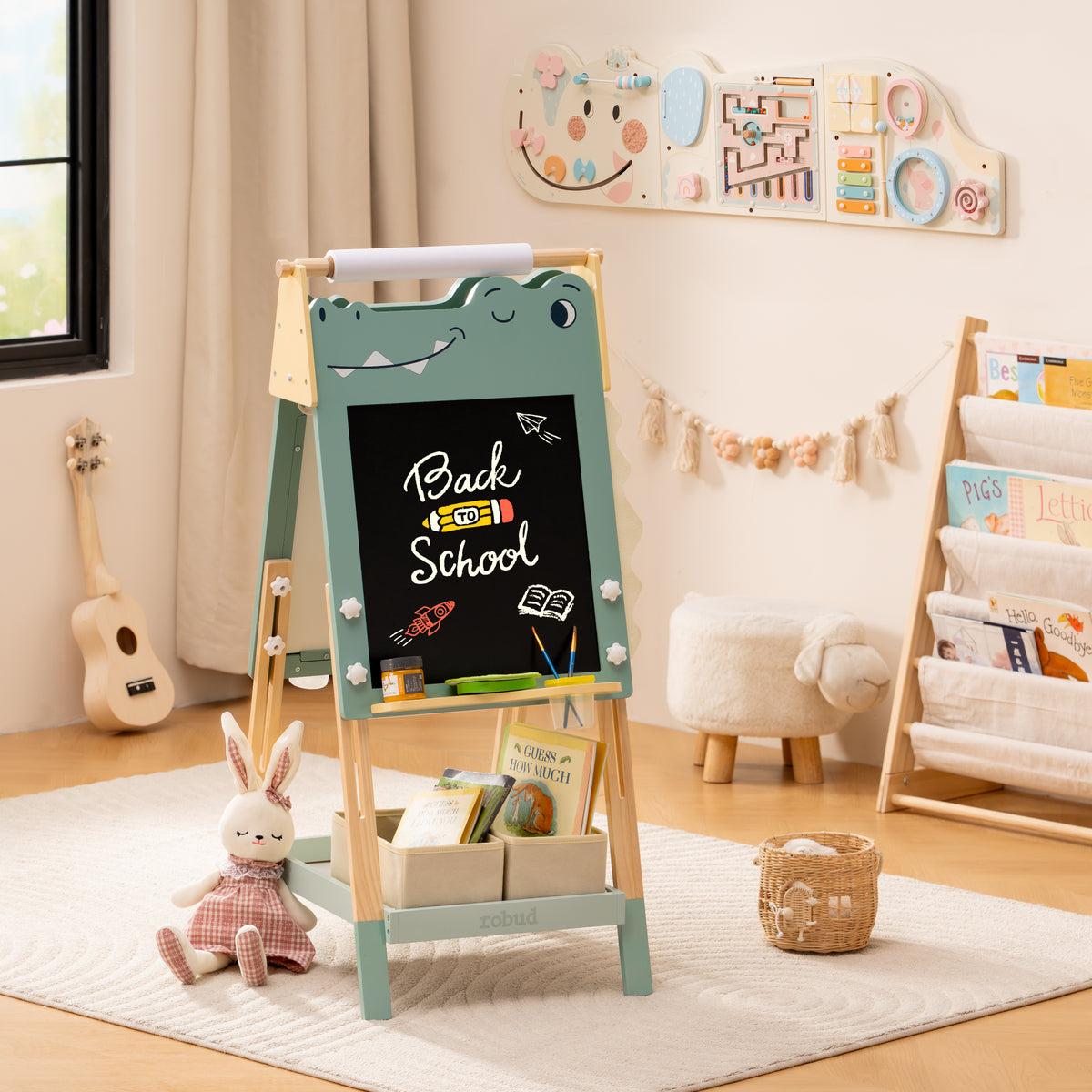 ROBUD dinosaur art easel with chalkboard side facing out shown in a light playroom with bookshelf in the background.