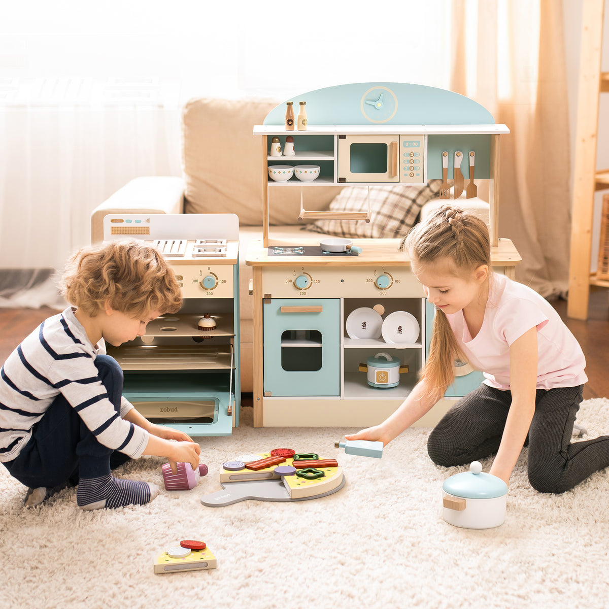 Two children playing together on the floor with Robud green kitchen and oven set in a cosy room