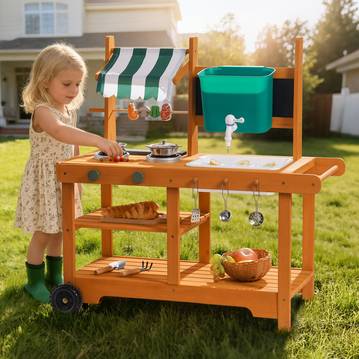 Smiling girl in hat at ROBUD wheeled outdoor mud kitchen on green lawn with stainless steel pots and natural wood countertop