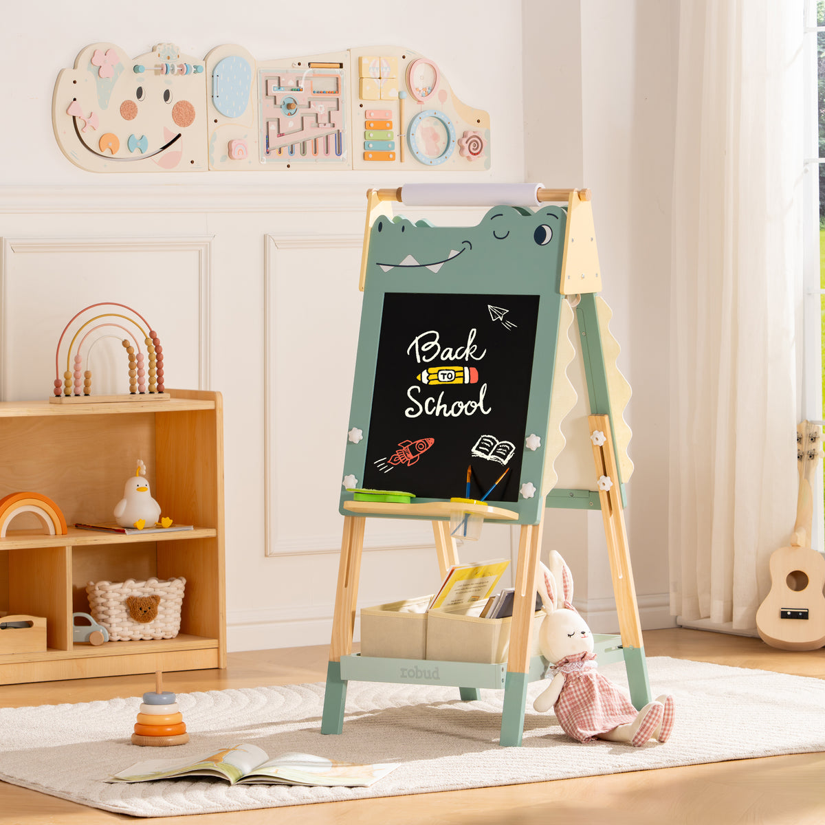 ROBUD dinosaur chalkboard easel with Back to School chalk text positioned in a bright neutral playroom with bookshelf.