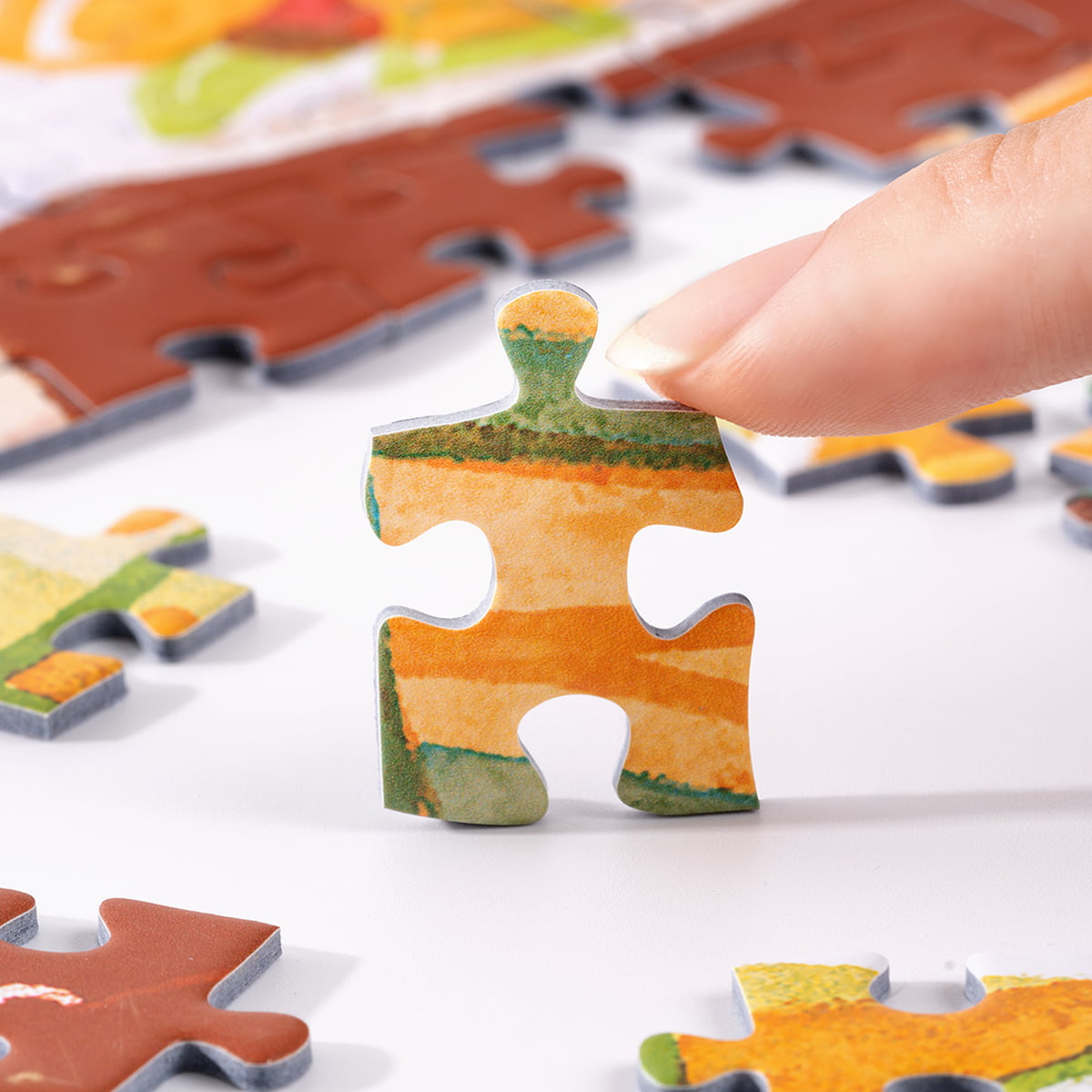 Hand picking up a Rolife Amalfi Holiday PT005 puzzle piece showing orange and green illustrated Mediterranean landscape tones