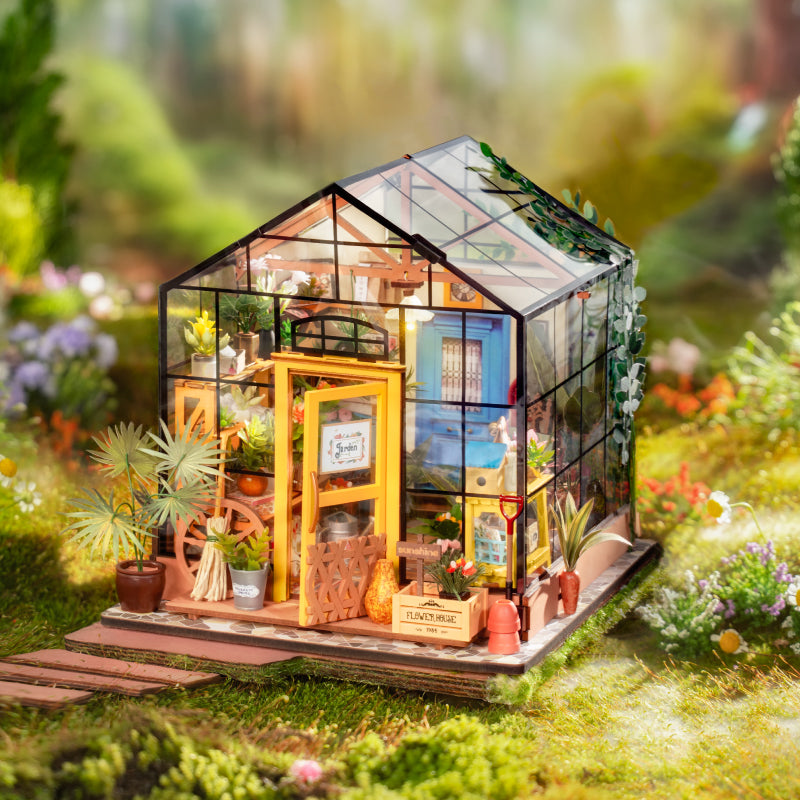 Rolife dollhouse miniature kit shaped like a glass greenhouse cottage with garden furniture, set among grass and flowers