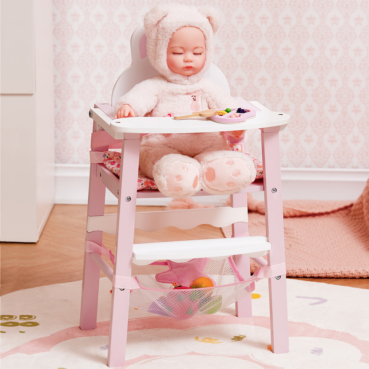 ROBUD pink wooden doll high chair with baby doll seated inside, photographed against a delicate floral pink wallpaper.