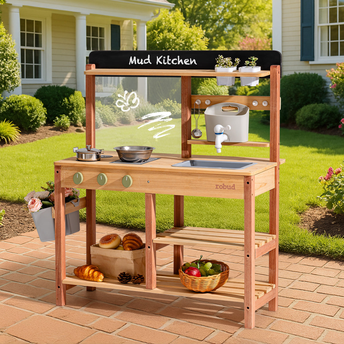 ROBUD outdoor wooden mud kitchen with chalkboard sign, metal sink, water dispenser, and lower shelves holding bread and a basket of fruit