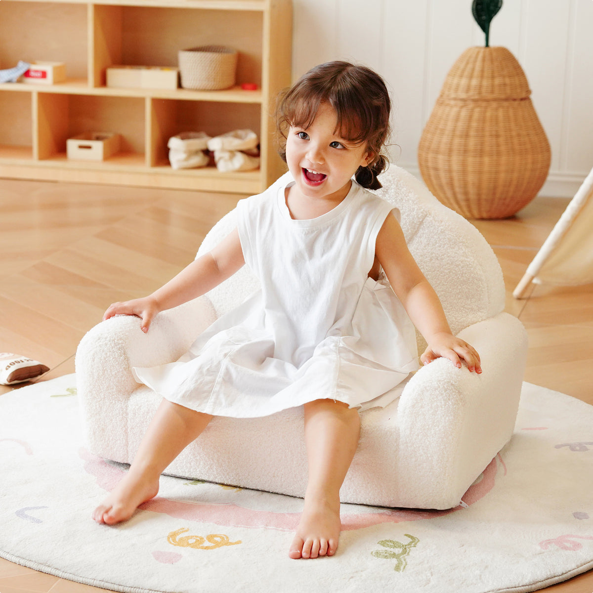 Young girl sitting alone on the ROBUD cream Children's Sofa in a warm Scandi-style playroom with natural light