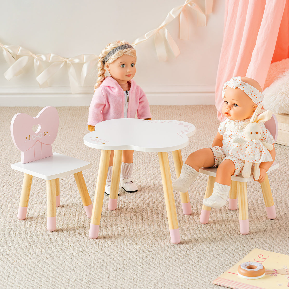 Young girl and baby doll seated together at ROBUD pink heart-back chair and white round table in a warm pastel room setting