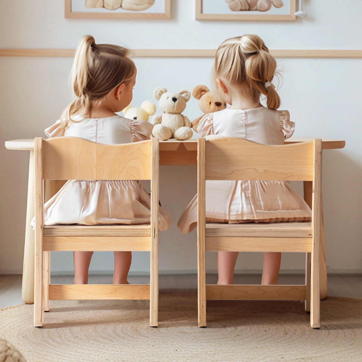Two girls in matching dresses sitting with their backs to camera at ROBUD natural wood toddler table and chairs with stuffed animals on the table