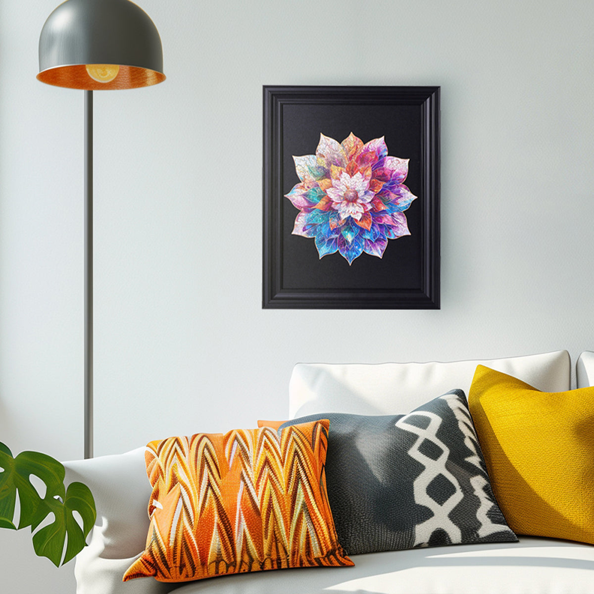 Rowood Mystic Mandala Flower wooden puzzle displayed in a black frame on a living room wall above a sofa with orange and yellow cushions.