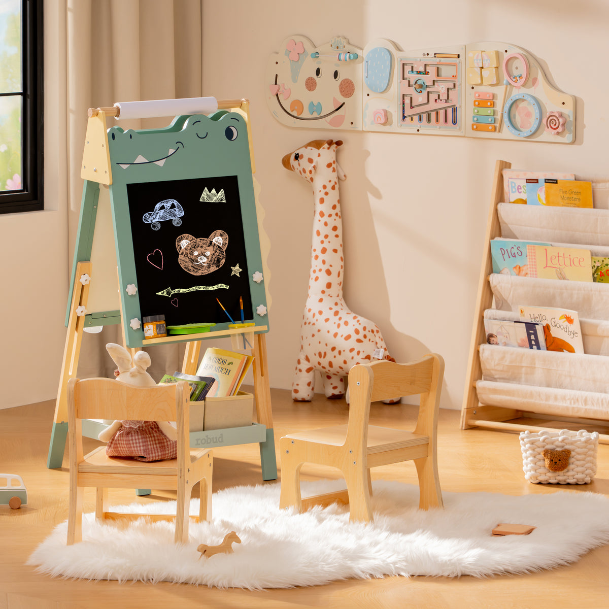 ROBUD dino easel and natural wood storage shelf in a pale playroom with a fluffy white rug and stuffed giraffe nearby.