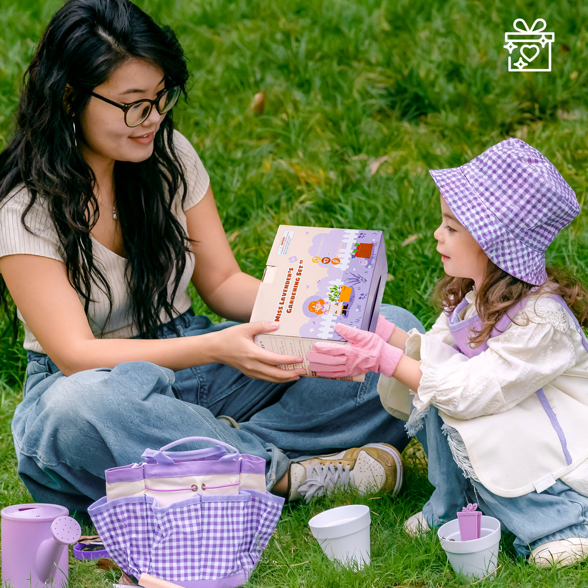 Mother sitting on grass helping young child explore ROBUD Kids Gardening Set purple series tools and accessories outdoors