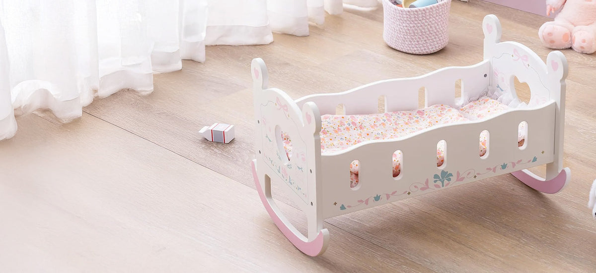 ROBUD white and pink wooden doll changing station with baby doll, pink gingham mattress, hanging wardrobe curtain, storage drawers, and decorative hat displayed in a nursery