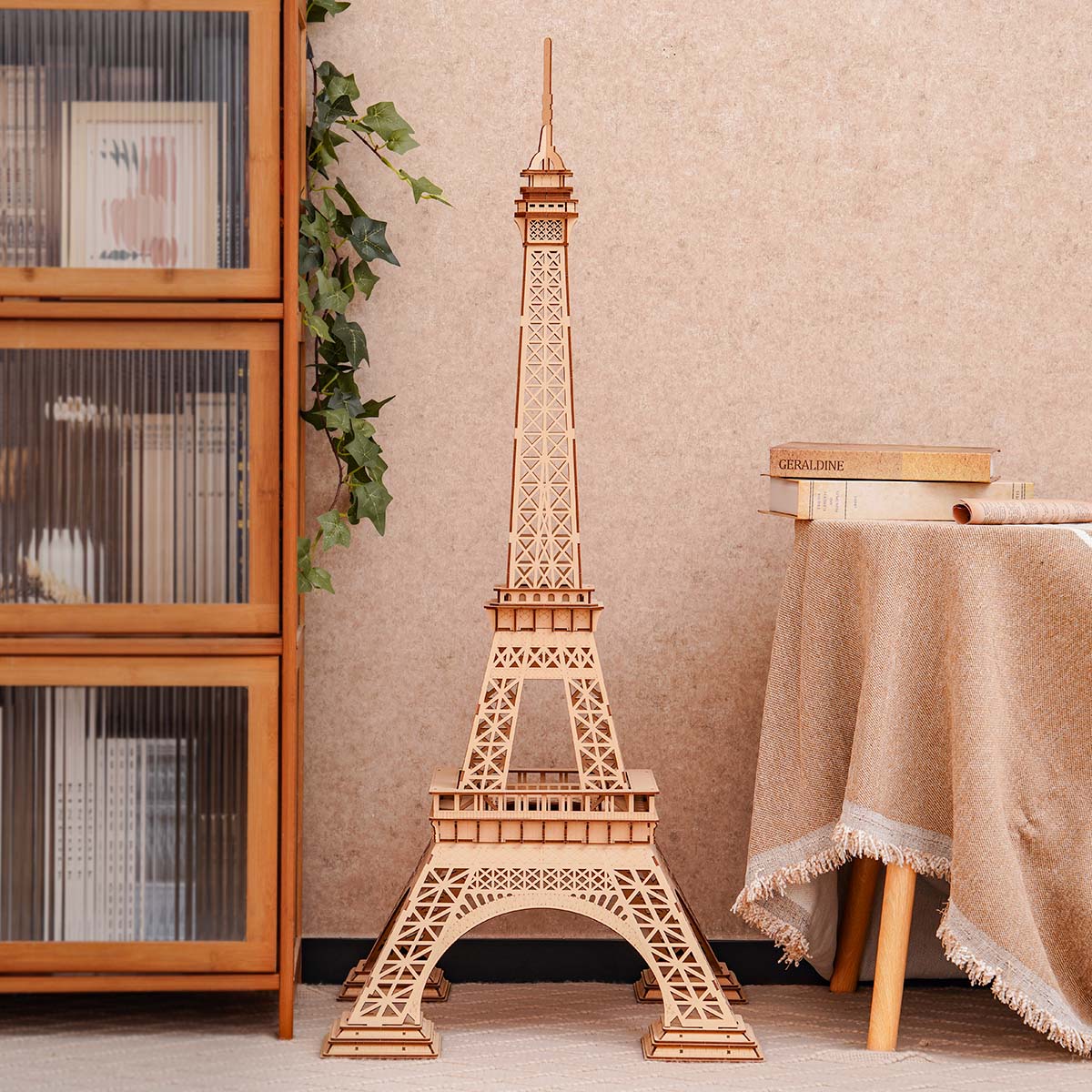 Rolife Eiffel Tower Plus wooden model standing beside a cabinet and small round table.