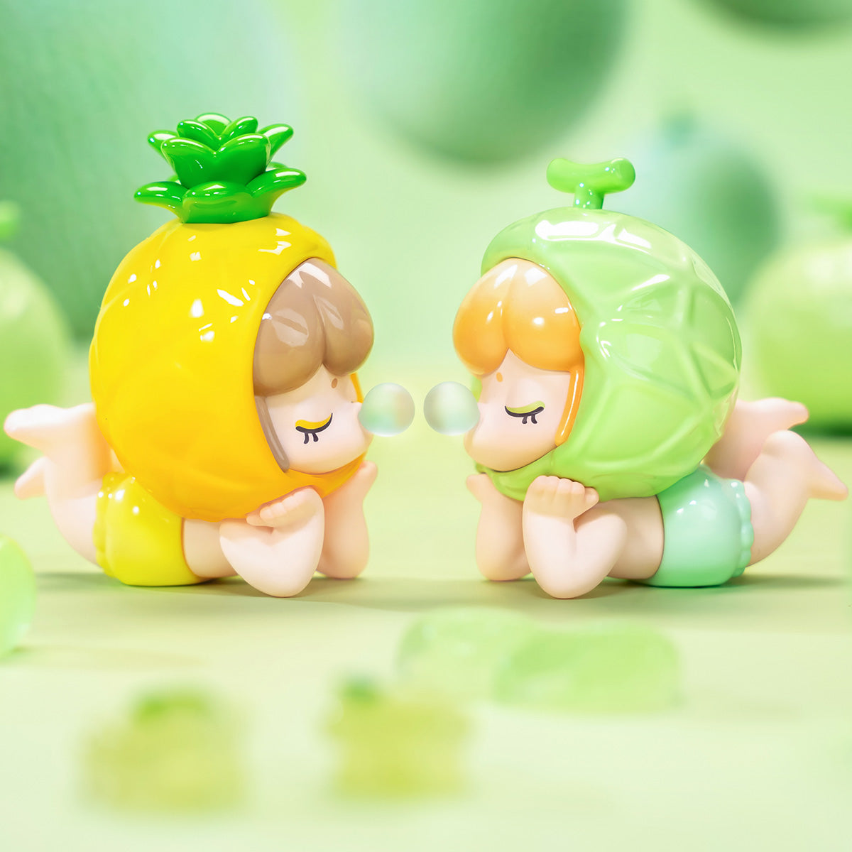 Rolife Baby Nanci Fruits pineapple and cantaloup costume figures face to face on a green background as if sharing a bubble gum bubble in a playful green lifestyle scene
