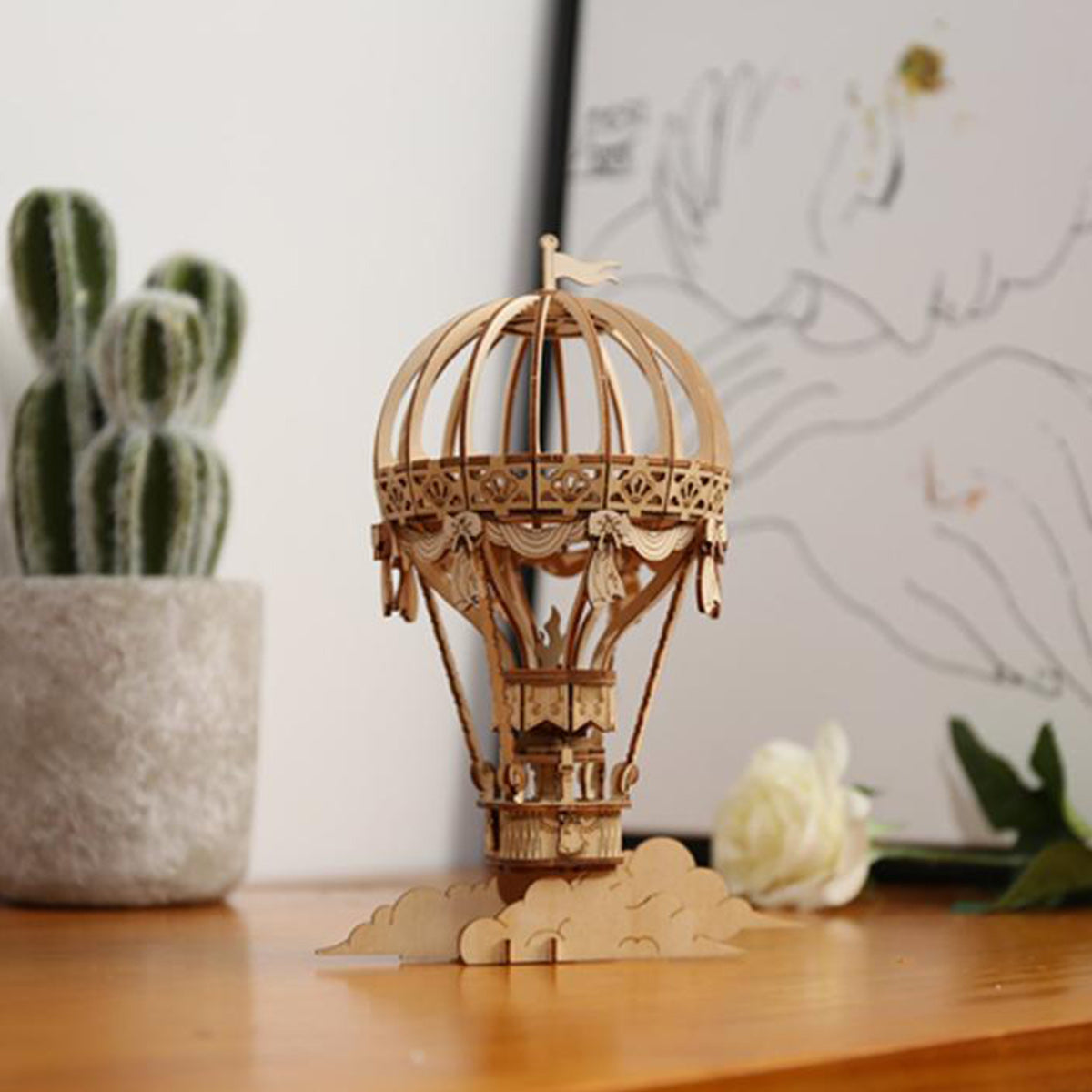 Assembled Rolife hot air balloon 3D wooden puzzle on a shelf beside a cactus plant and white flower