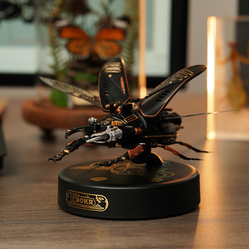 ROKR Storm Beetle MI03 mechanical beetle on desk beside warm lamp glow and framed butterfly art