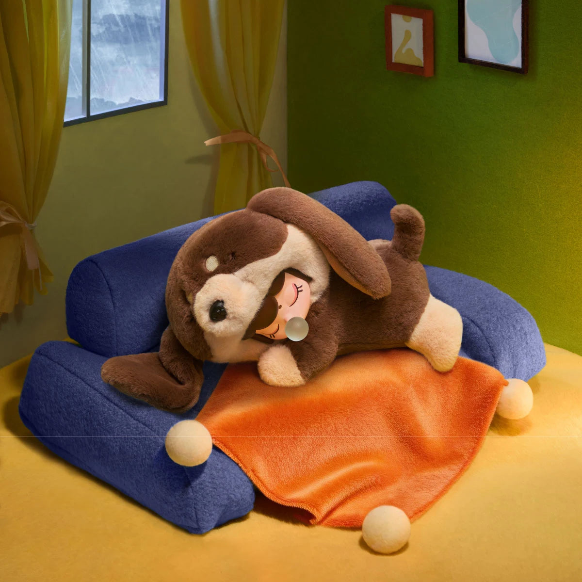 Brown and cream plush puppy toy with a doll face lying on a blue cushion and orange blanket, with small white balls and a rainy window behind.