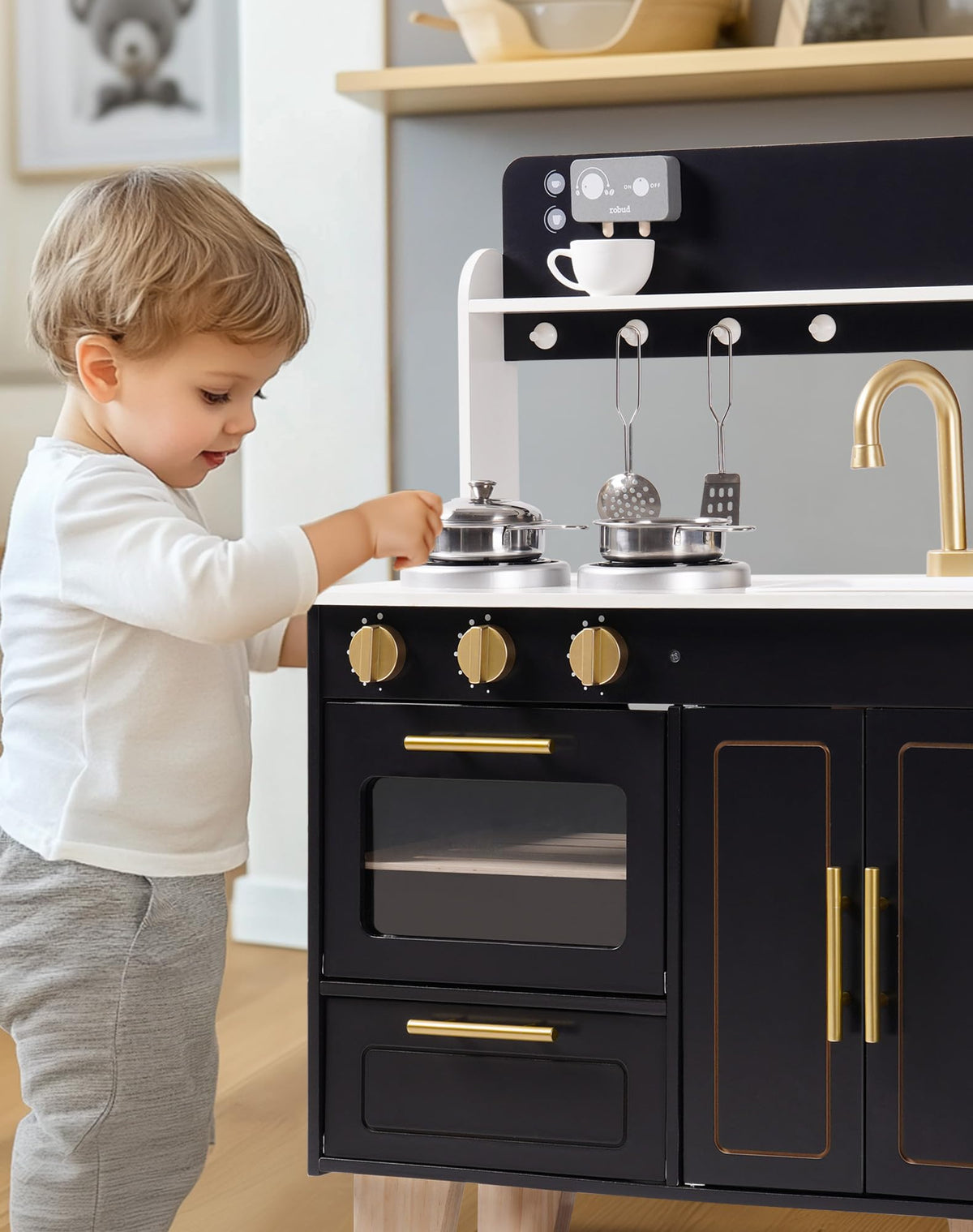 Young boy opening oven door on ROBUD obsidian wooden kitchen playset with gold accents in light-filled room