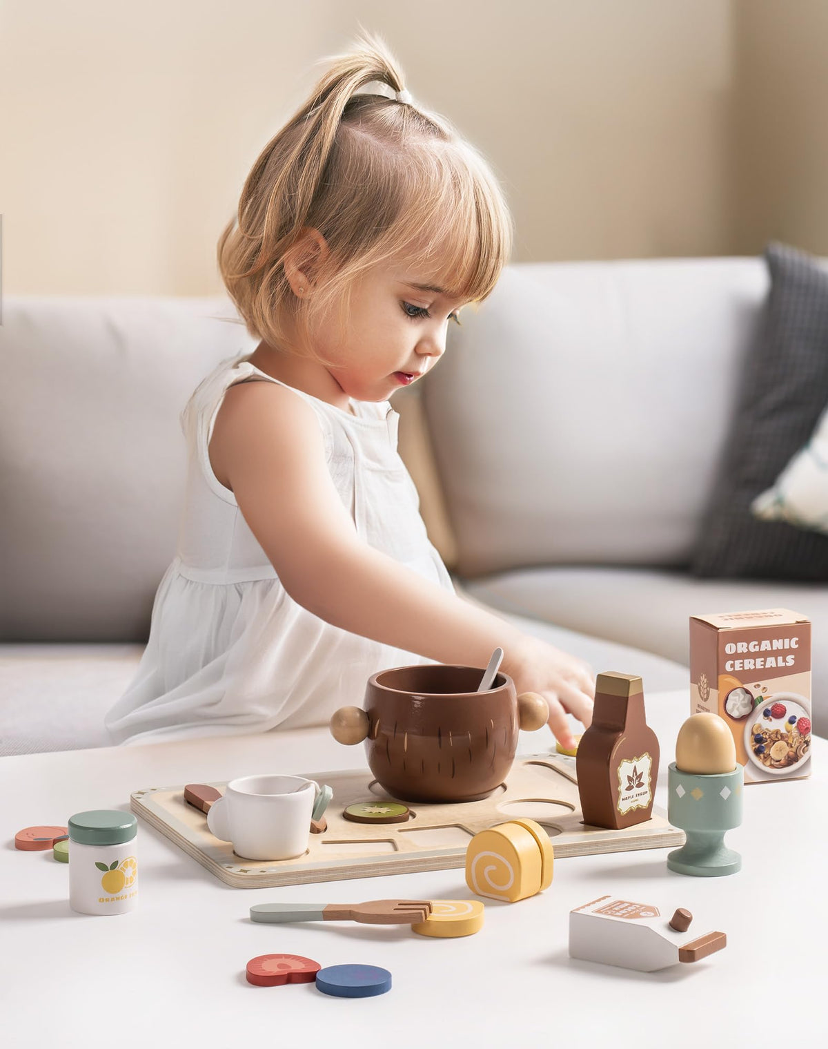 Young girl playing with ROBUD wooden breakfast food set on floor with bowl and tray in cozy living room