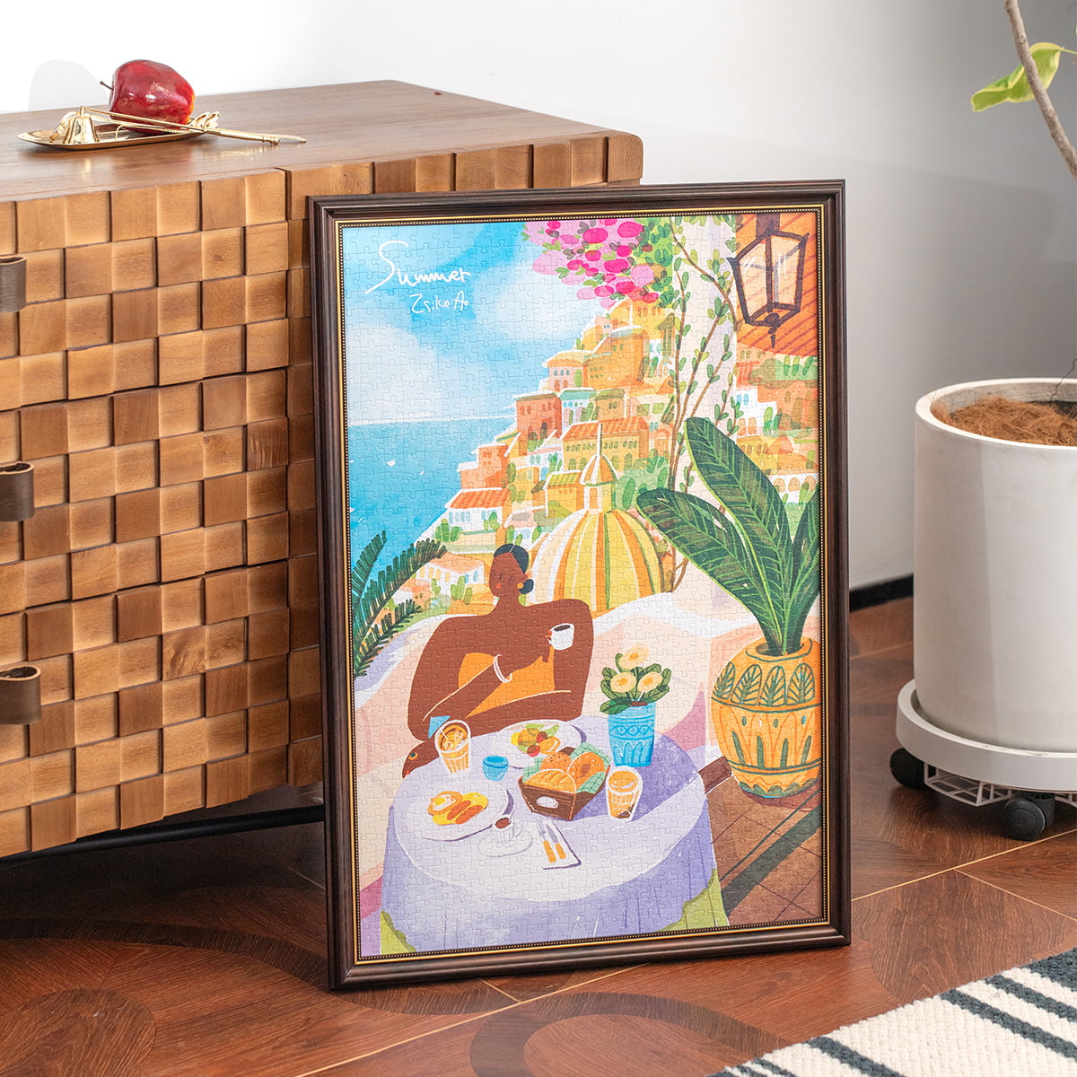 Rolife Amalfi Holiday PT005 completed puzzle in black frame displayed on wooden sideboard beside a coffee cup and plant