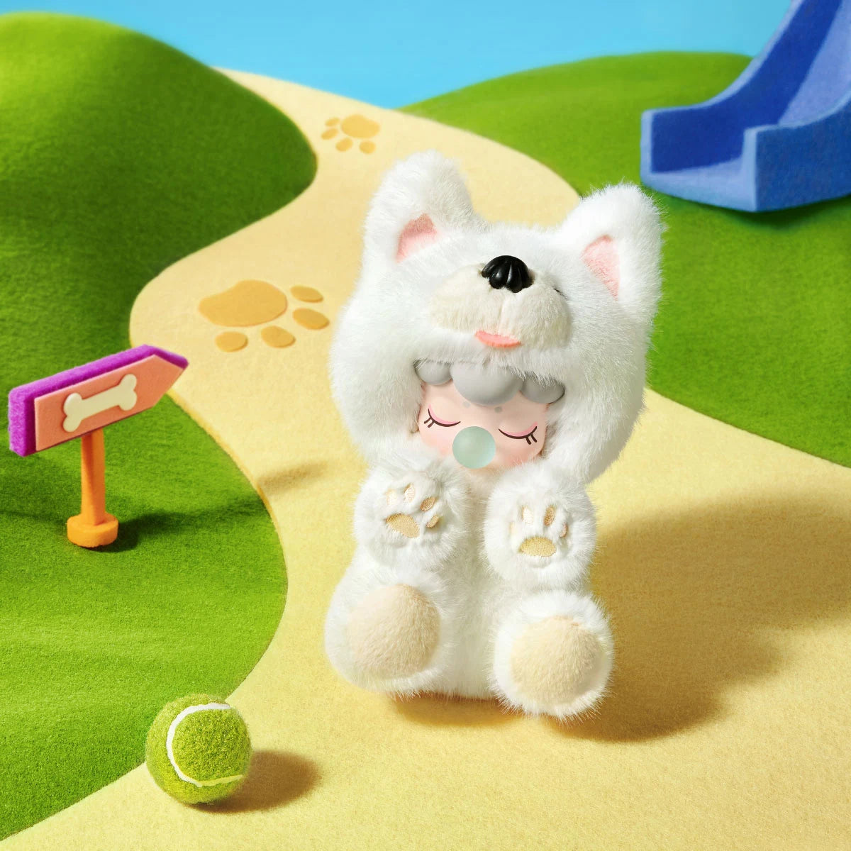 White plush dog toy with a doll face sitting on a yellow path with paw prints, beside a bone sign, green tennis ball and blue slide.
