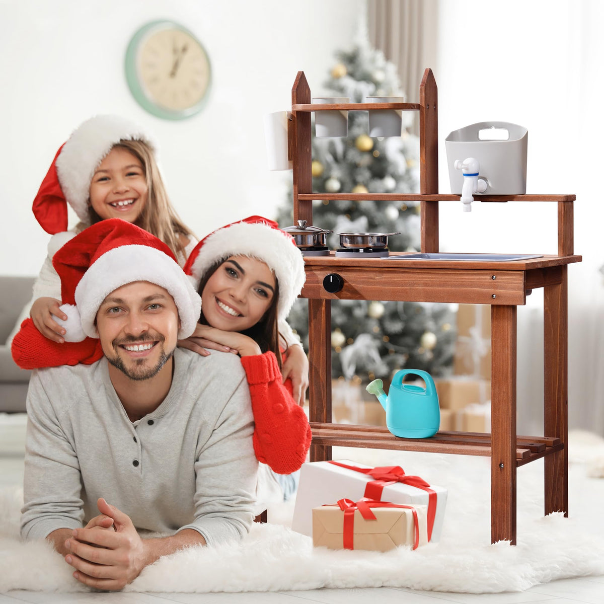 Family wearing Santa hats posing beside a ROBUD brown outdoor mud kitchen in a festive Christmas living room setting