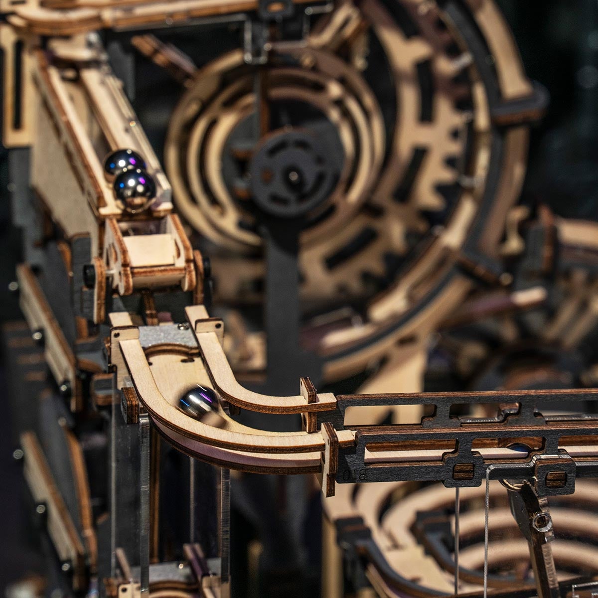 Macro detail of a steel marble on a curved rail of ROKR Marble Night City with a large wooden gear wheel visible above