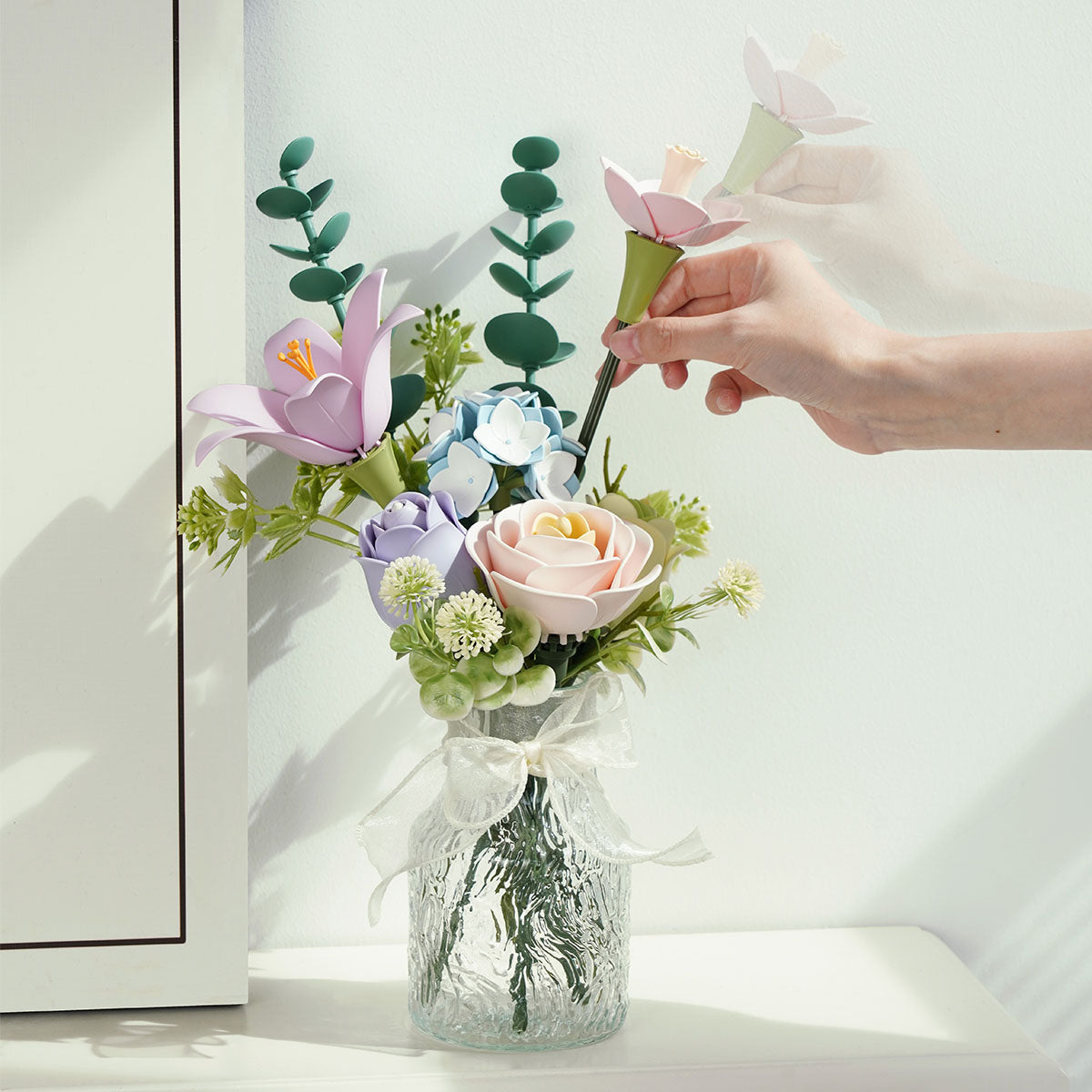 Hand places stems into a clear vase for the ROKR Spring Time Bouquet near a mirror.