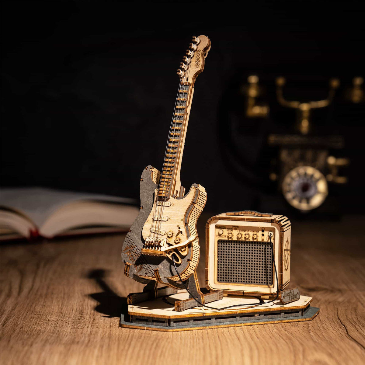 ROKR wooden electric guitar model beside a mini amp on a dark desk with vintage clock and open book backdrop