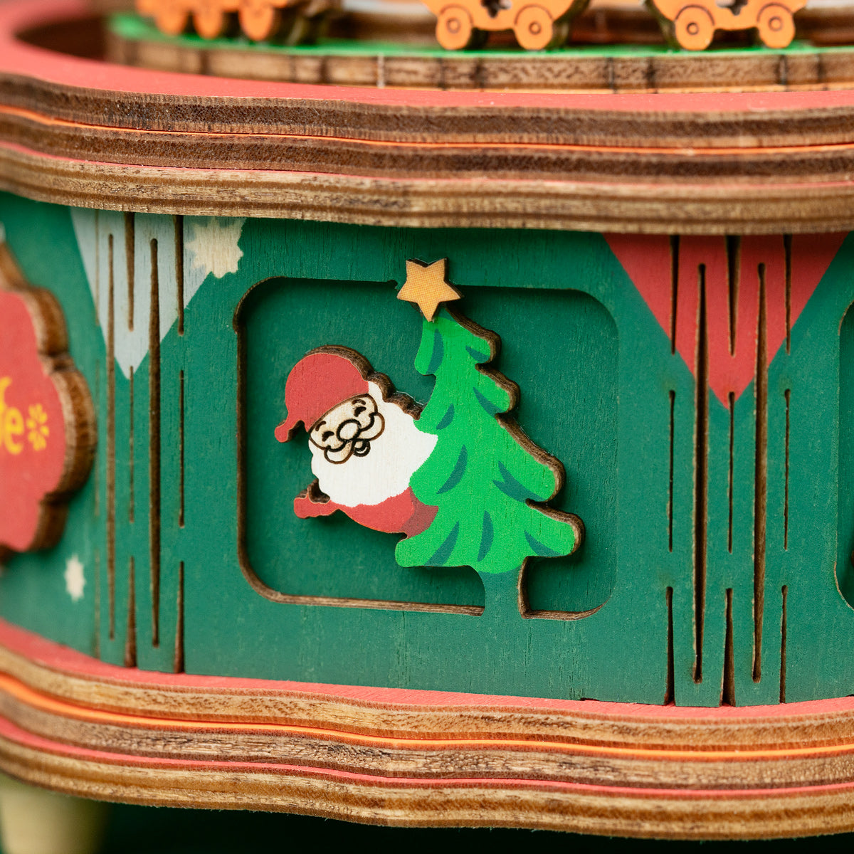 Rolife Christmas Snow Globe AM46 close up of the Santa Claus carving on the festive green and red octagonal wooden base with holiday motifs