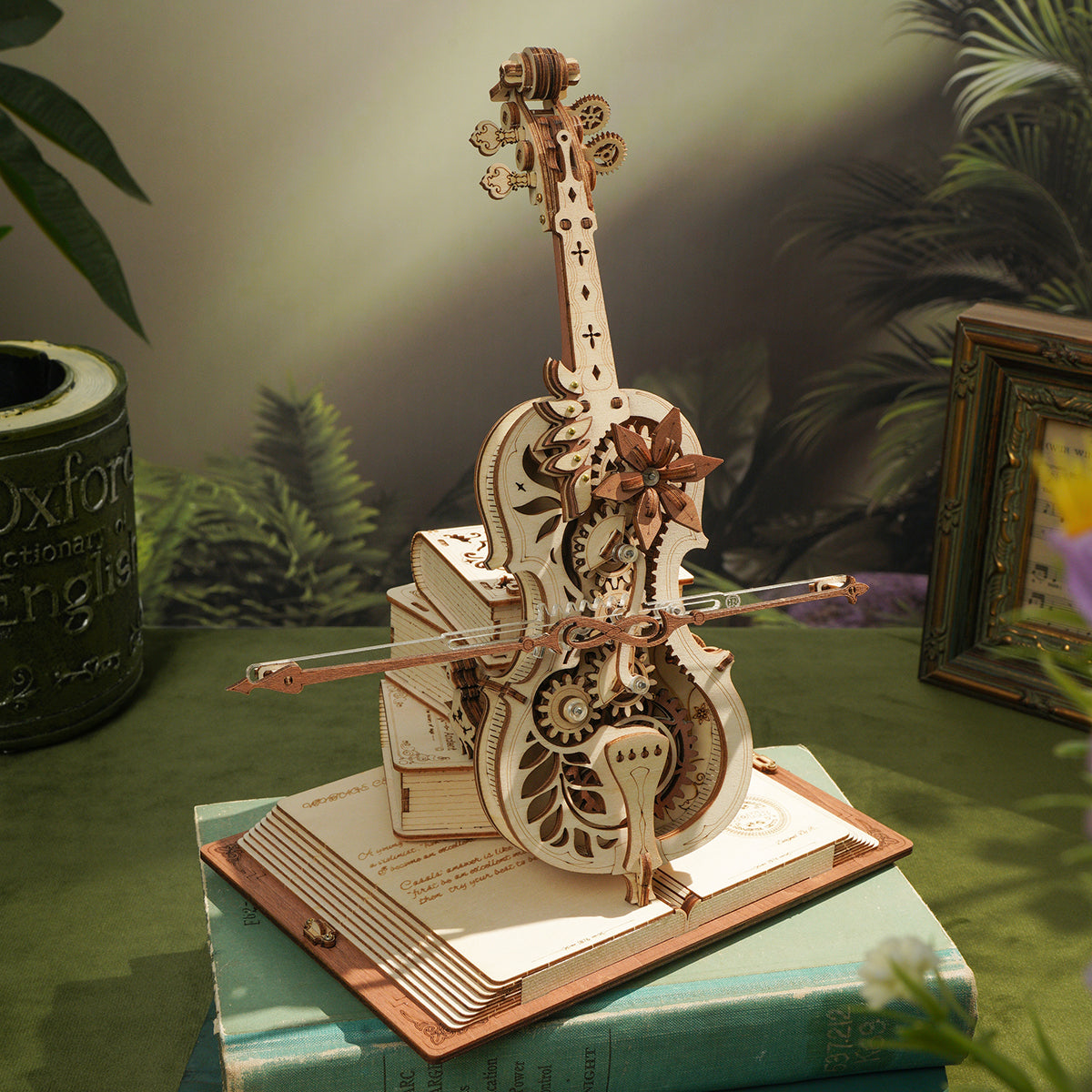 ROKR wooden cello music box with exposed gear mechanism on an open-book base against a lush green tropical backdrop