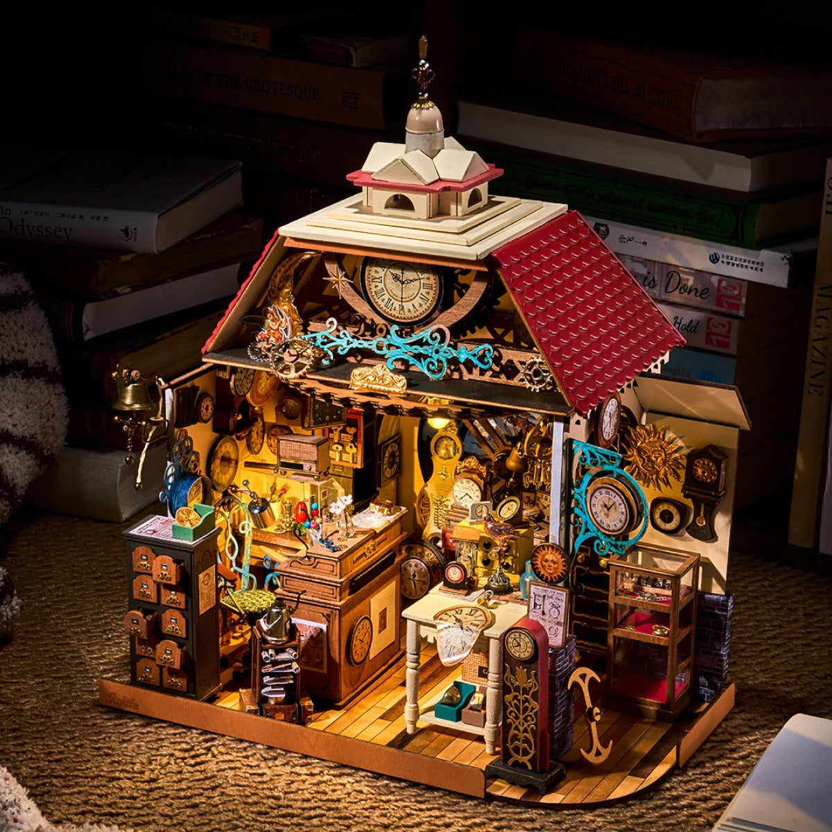 Rolife miniature clock shop lit warmly on a textured surface, surrounded by stacked books, showing red roof, clocks and detailed interior.