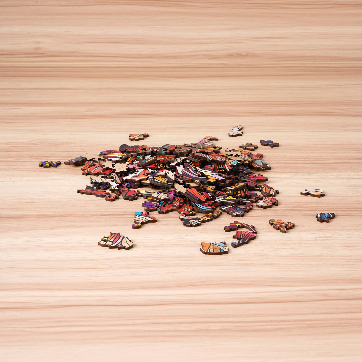 Rowood Cat King wooden puzzle pieces scattered across a light wooden surface before assembly, revealing colorful fur-pattern fragments.
