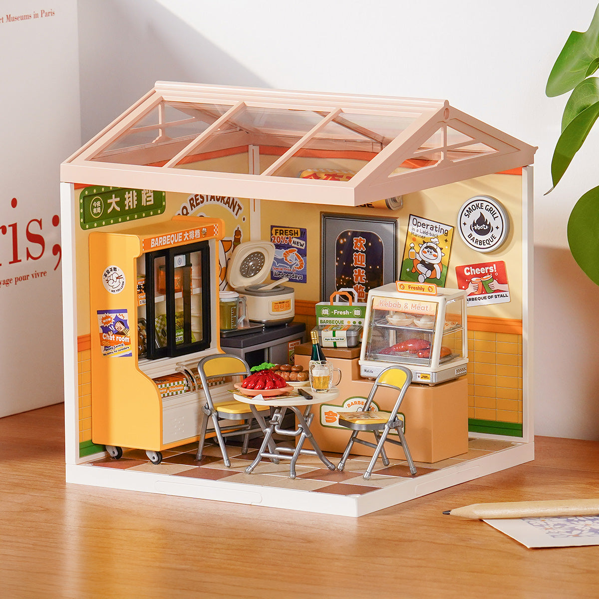 Rolife Night Out Food Stall DW022 Super Creator miniature house displayed on a desk showing a yellow barbeque street food stall with folding chairs and signage