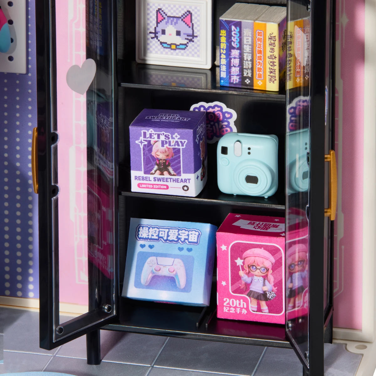 Miniature black display cabinet with glass doors and gold handles, holding tiny boxes, a pixel cat picture, books and a mint-green instant camera on shelves.