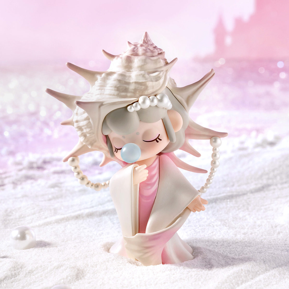 Pastel pink figurine wearing a seashell crown with pearls, standing on sand against a sparkly backdrop