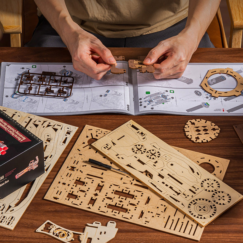 Hands assembling a ROKR Justice Guard mechanical wooden model with laser-cut sheets, tool, and illustrated instruction booklet spread across a wooden table
