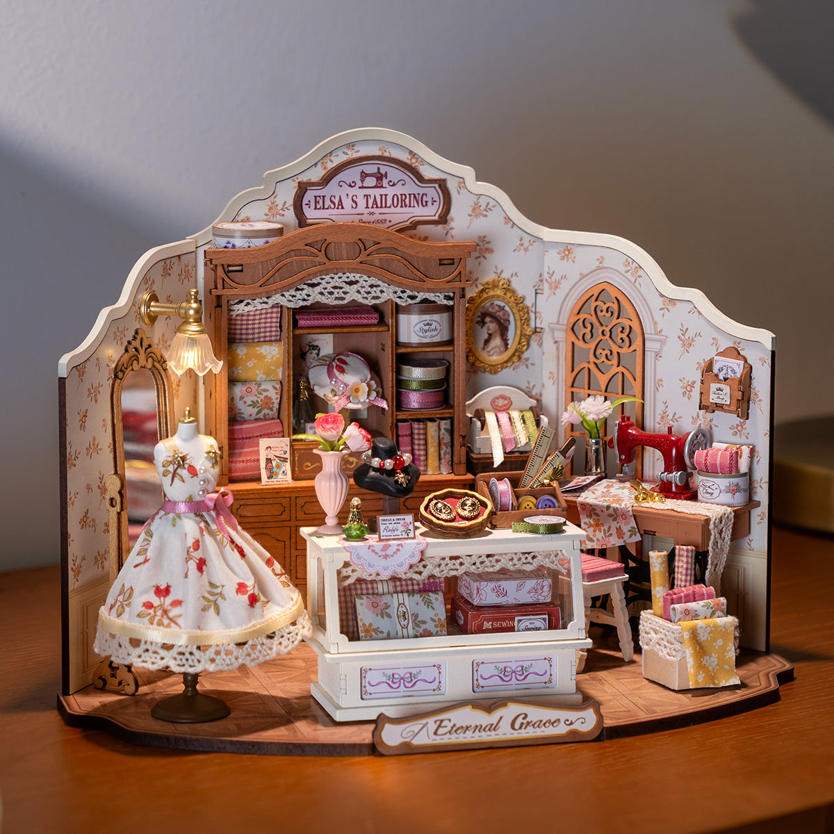 Rolife Elsa's Tailoring DG178 miniature tailor shop placed in a garden at dusk with pink sky, mannequin in floral dress and all interior details visible
