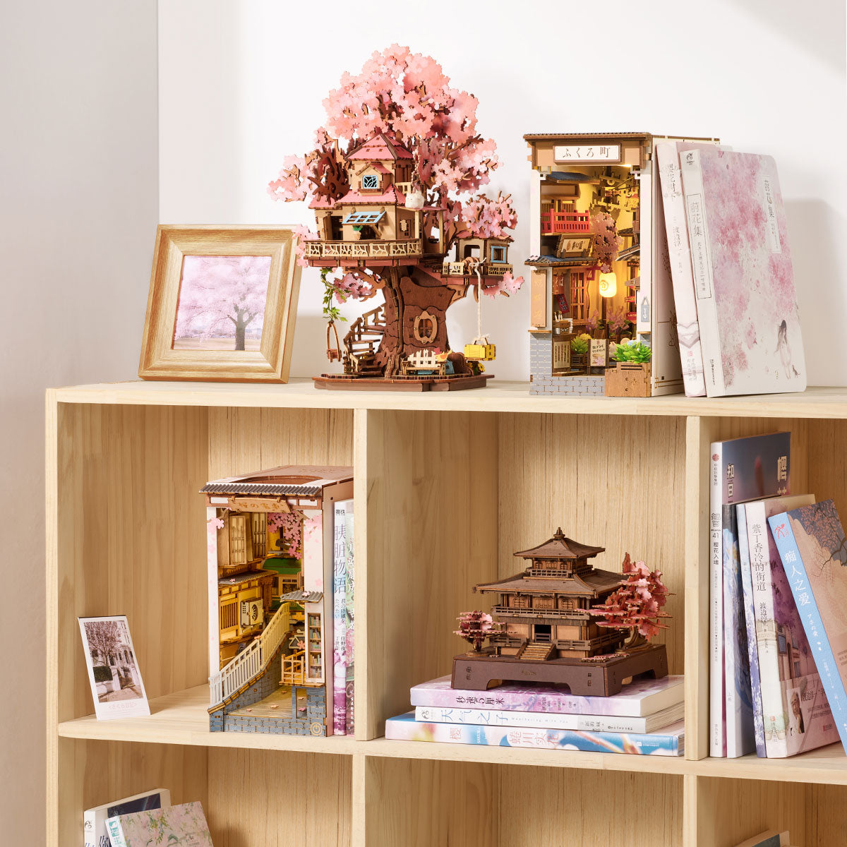 Rolife cherry blossom wooden puzzle collection including Sakura Pavilion pagoda and book nook styled on a light oak bookshelf with pink blossom prints and stacked books