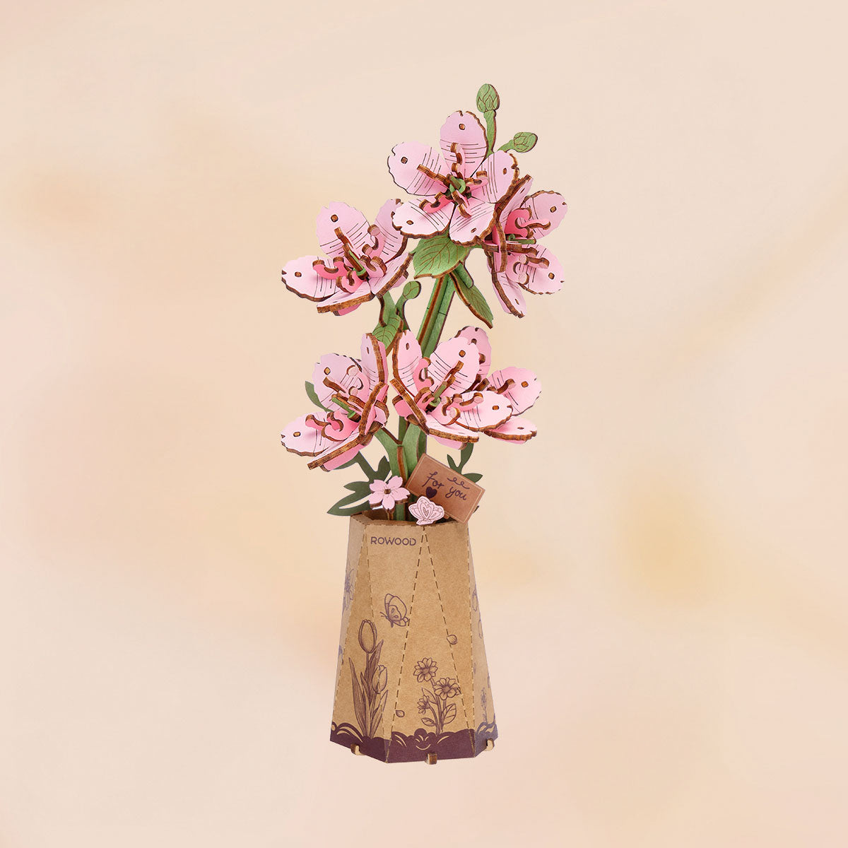 Rowood DIY wooden flower bouquet TW101 completed cherry blossom model showing full pink sakura branch arrangement in a kraft paper pot on a peach background.