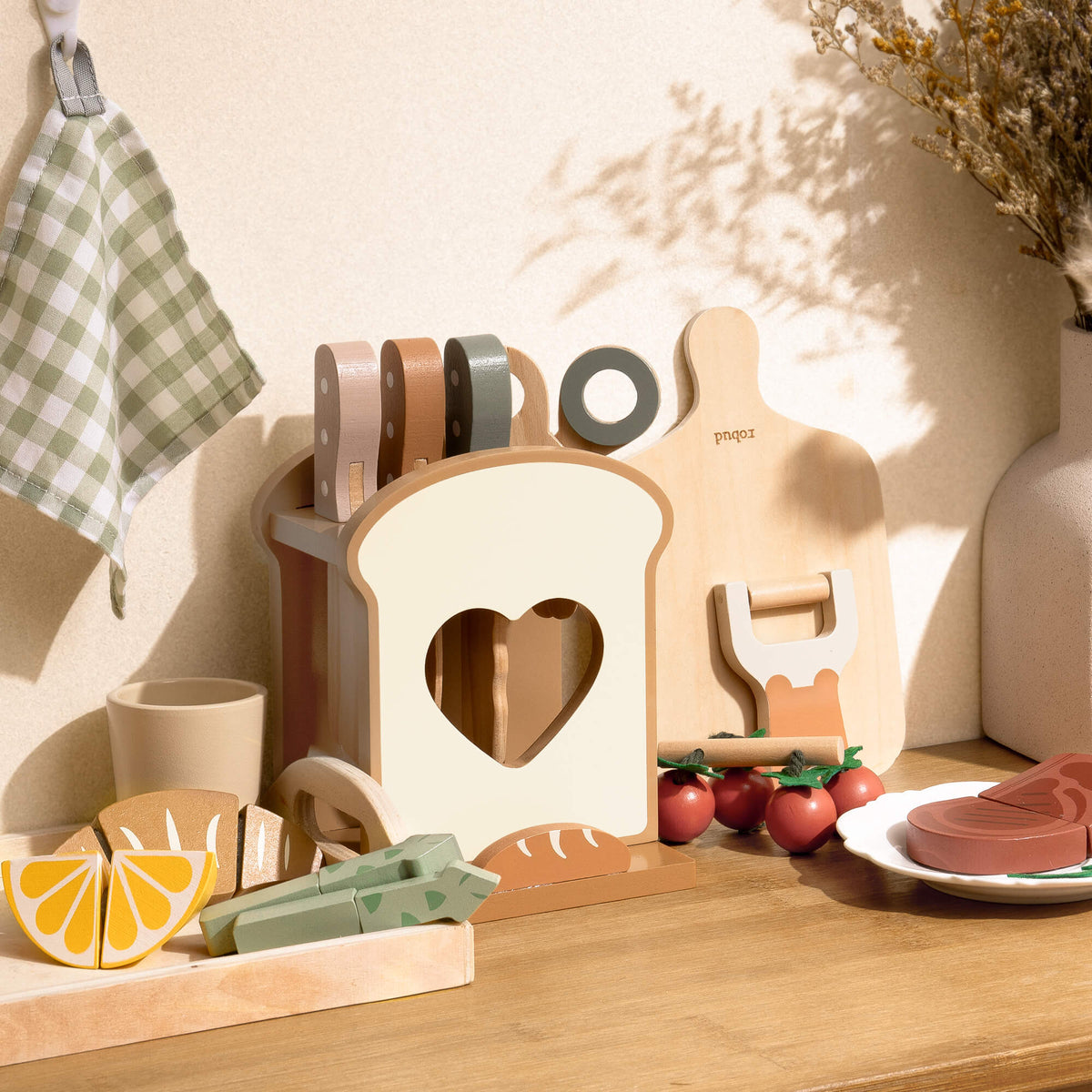 ROBUD Mocha Cookware Set wooden toy kitchen accessories displayed on a warm-lit table with toast holder, cutting board, steak, lemon halves and scattered food pieces