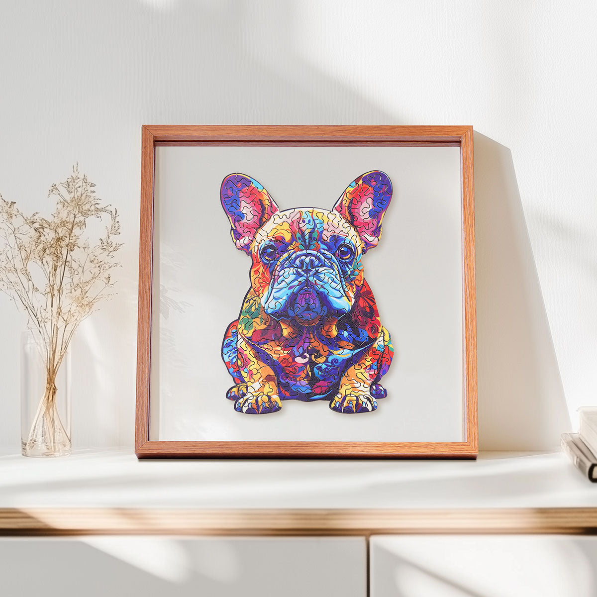 Rowood French Bulldog wooden jigsaw puzzle in a shadow box frame resting on a shelf beside a glass vase of dried flowers and a candle