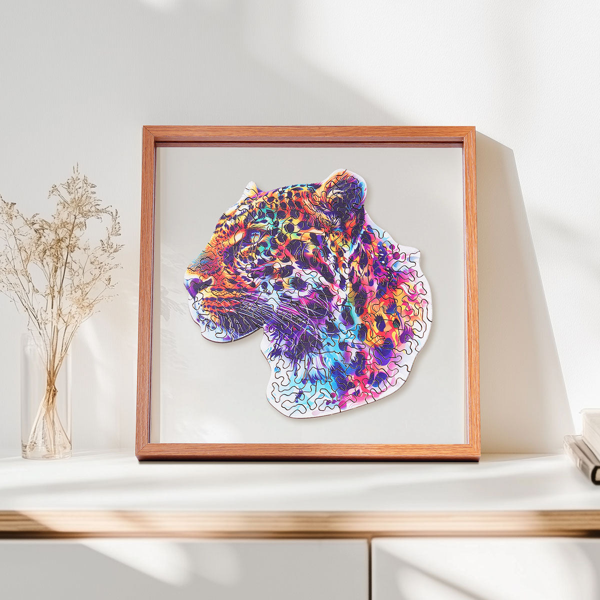 Rowood Fancy Leopard colorful wooden jigsaw puzzle in a shadow box frame resting on a shelf beside a glass vase with dried stems