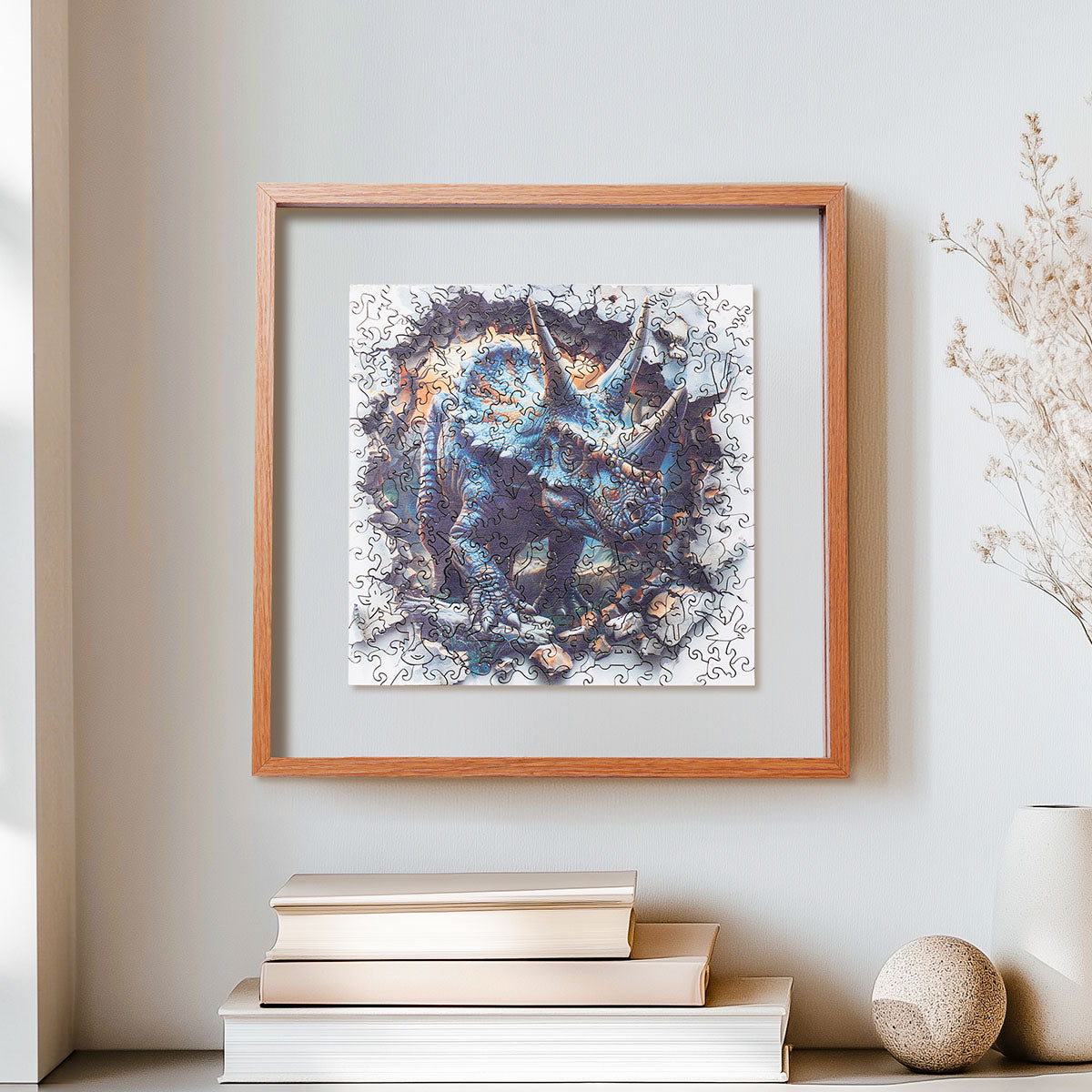 Rowood Wall Breaking Triceratops wooden jigsaw puzzle in a shadow box frame resting on a shelf beside dried flowers and a small book
