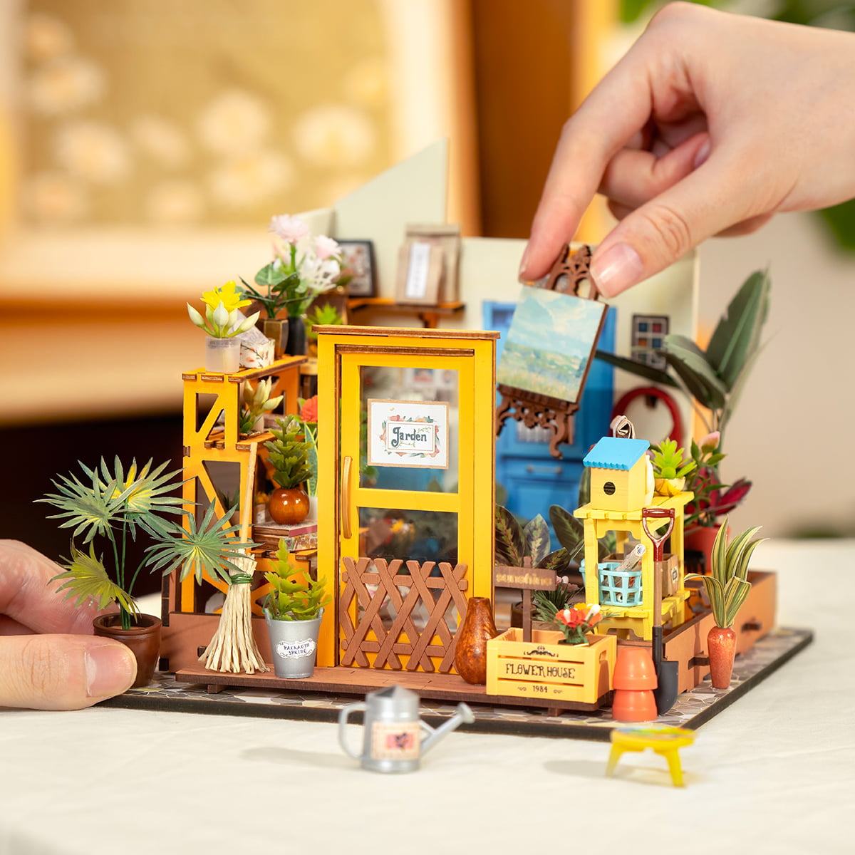 Hands placing small decoration into Rolife Cathy's Flower House miniature greenhouse scene on desk