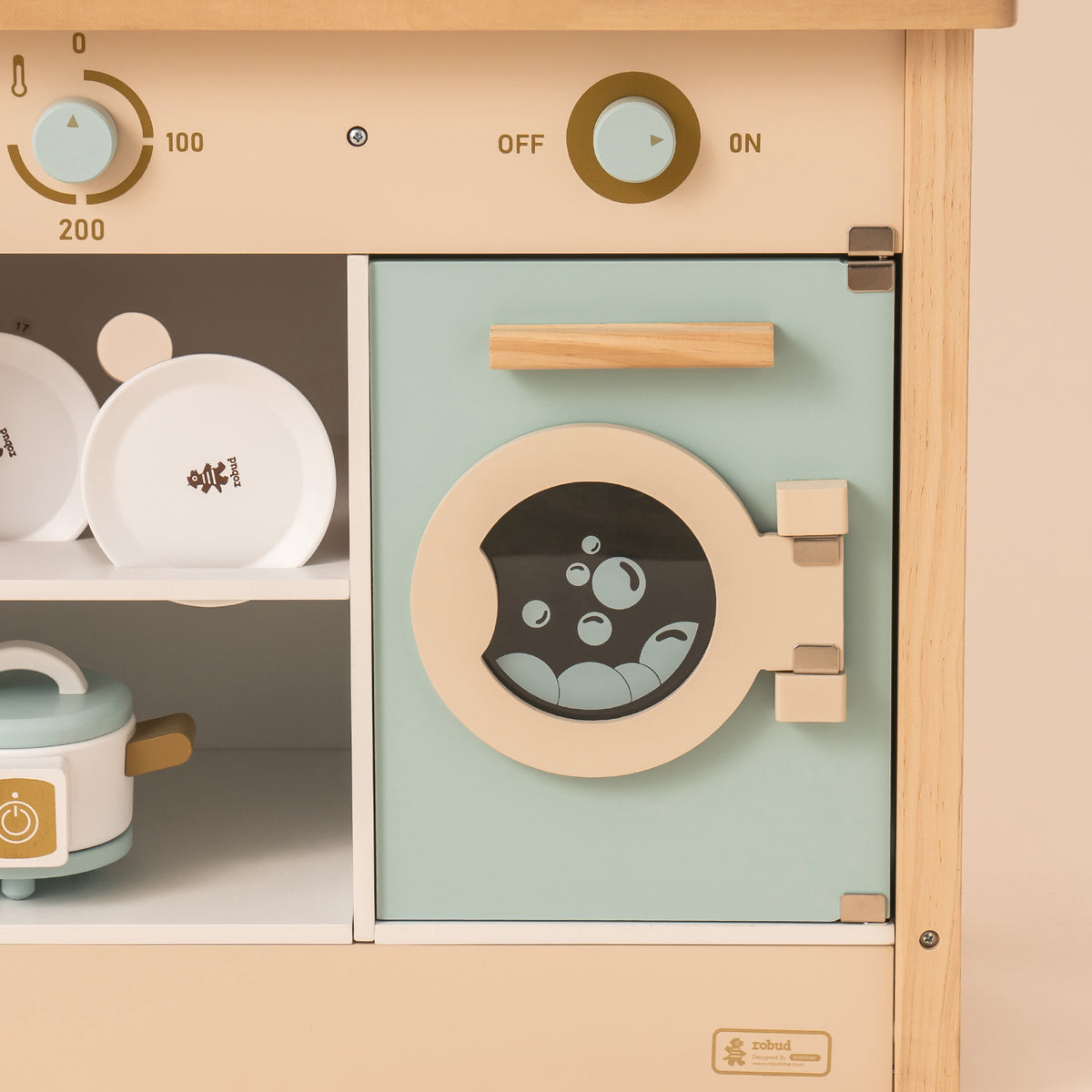 Child playing with ROBUD WCF14 mint wooden kitchen toy, kneeling and opening the washer door panel.