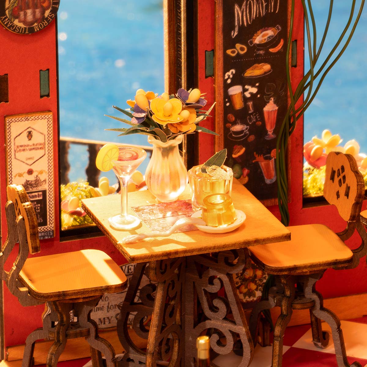 Rolife Cheers Bar DG173 miniature top-down interior view showing a cafe table with cocktail and flower vase, iron chairs, a chalkboard menu, and warm sunset lighting through the window
