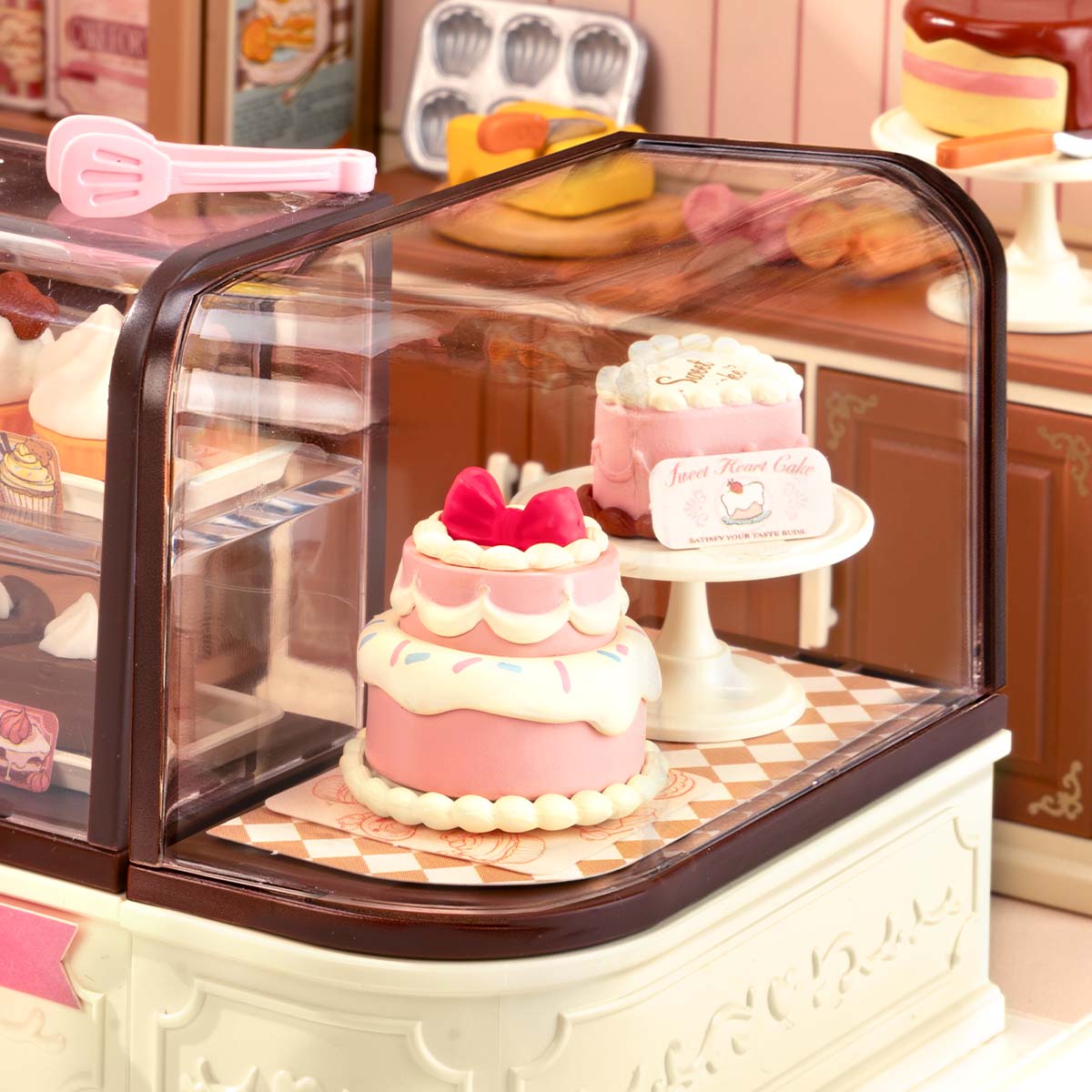 Rolife Tasty Cake Shop DIY miniature house DW019B displayed at an angle showing the fully assembled pink bakery interior with glass display counter, cakes, and warm LED lighting.