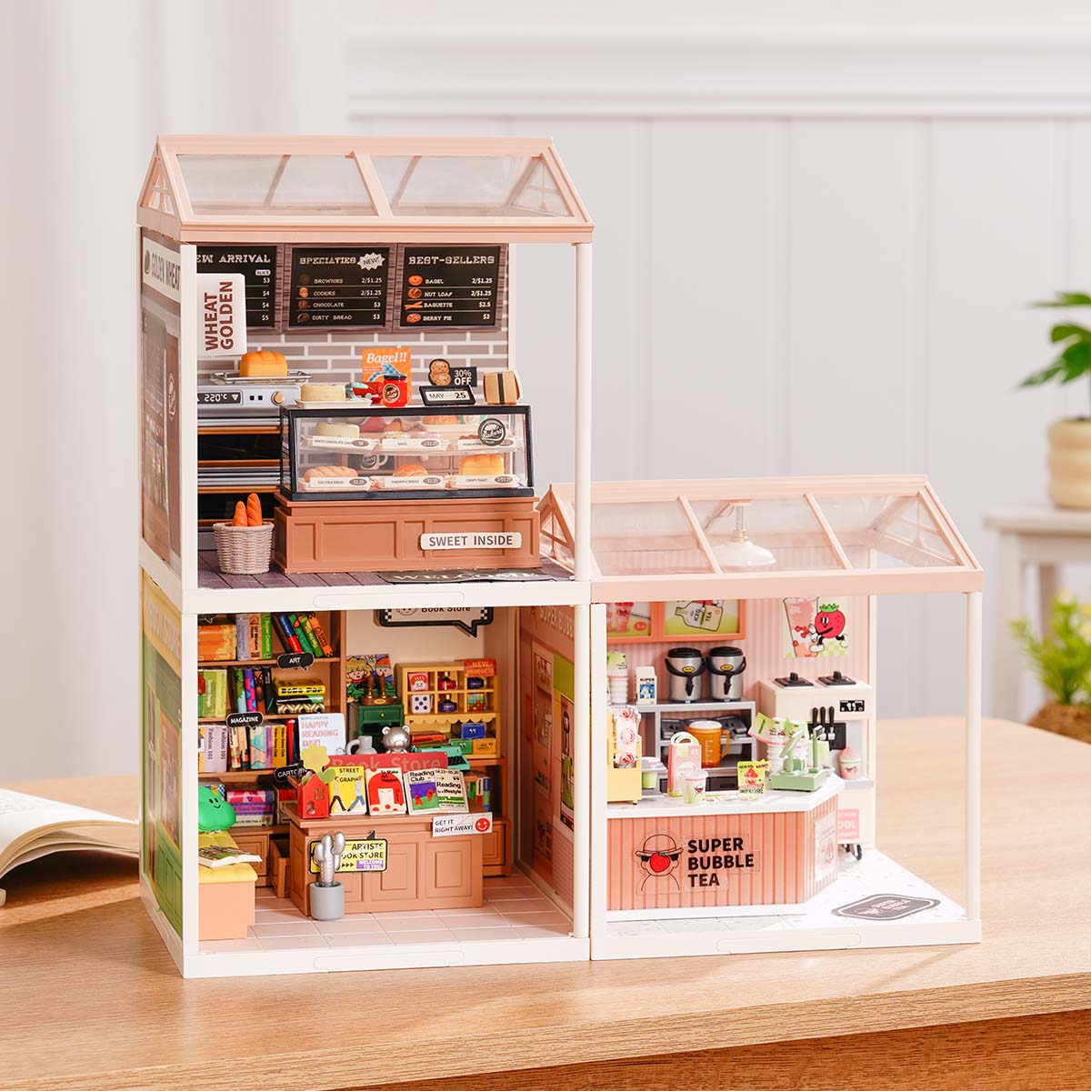 Rolife Super Creator Series 3-in-1 L Shape miniature with a tall bakery and a smaller bookstore and bubble tea room arranged in a wide L shape with a swing rooftop on a desk.