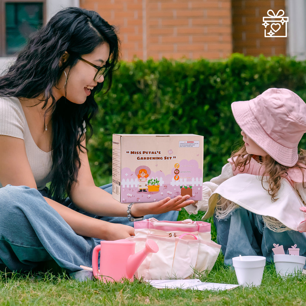 Girl in pink hat looking through ROBUD Kids Gardening Set magnifying glass in a lush green garden with pink gloves on her hands